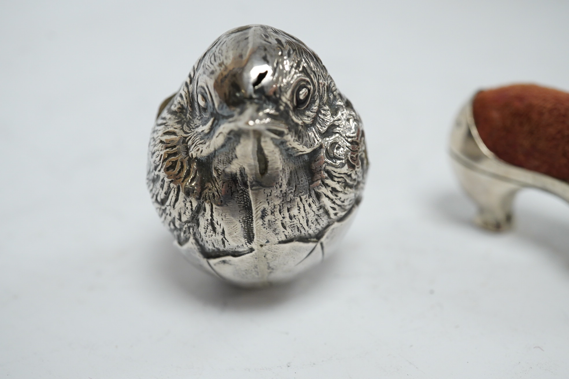 An Edwardian novelty silver pin cushion, modelled as a hatching chick, by Sampson Mordan & Co, Sheffield, 1906, height 43mm (hole), together with a late Victorian shoe pin cushion, by Adie & Lovekin, Birmingham, 1892, Co